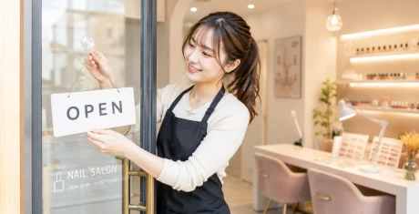 お店のドアに「OPEN」の札を掛けて、自分のお店を開店する笑顔の女性
